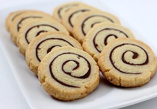 A rectangular white plate with neatly arranged spiral cookies featuring a light-colored dough and a dark chocolate swirl pattern.