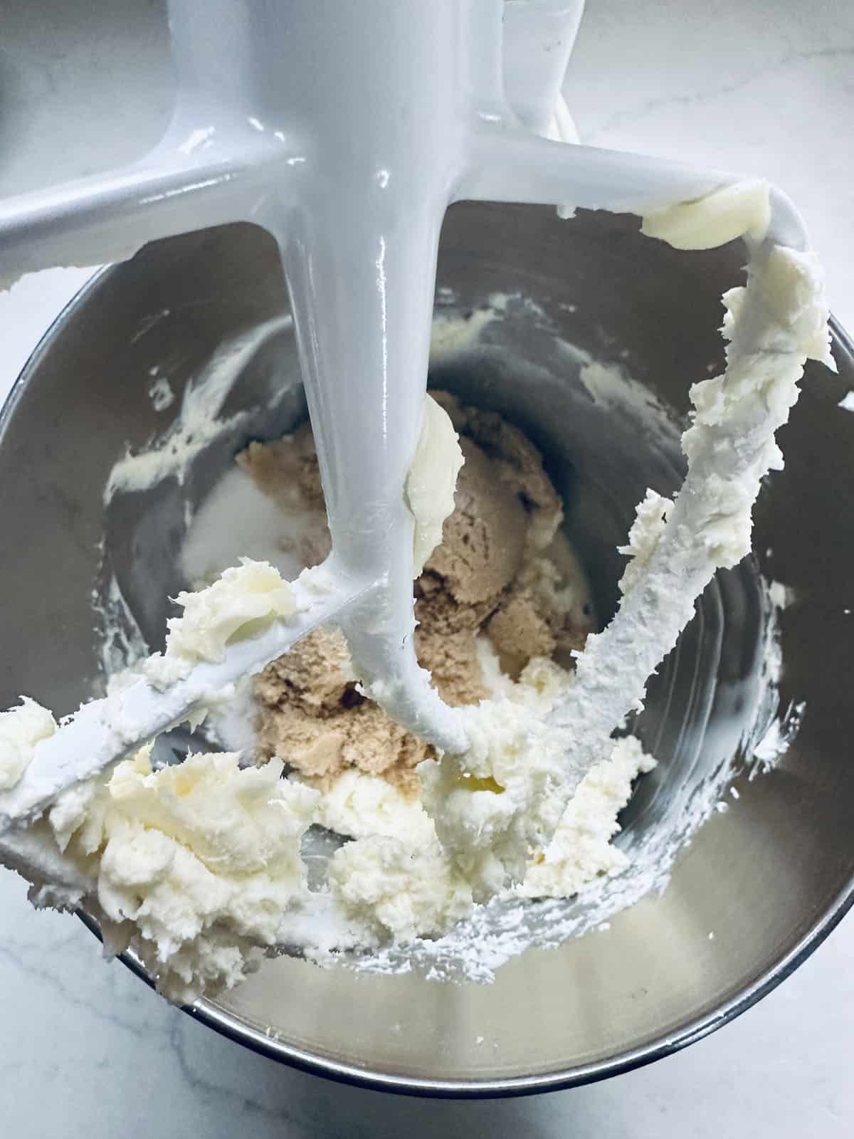 A mixer with a white mixer and white frosting in it.