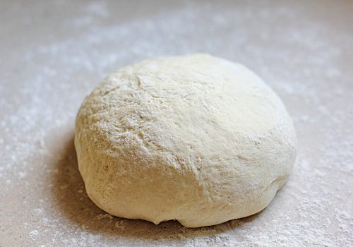 A ball of raw dough sits on a lightly floured surface, ready for baking or further preparation.