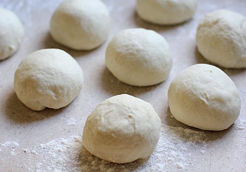 Balls of raw dough rest on a floured surface, arranged in rows, ready for baking or further preparation.
