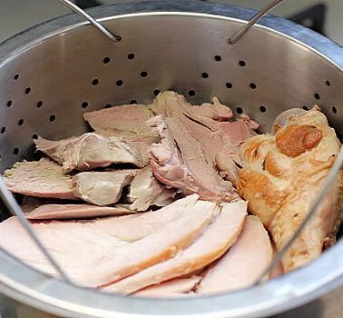 Sliced pieces of cooked turkey meat, including both white and dark portions, arranged in a metal steamer basket with perforated holes.
