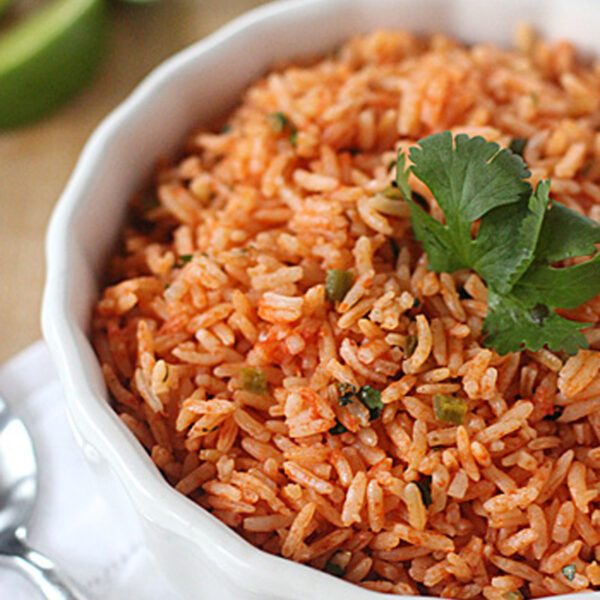 A bowl of Mexican rice garnished with cilantro, with lime wedges and a spoon on a white napkin nearby.