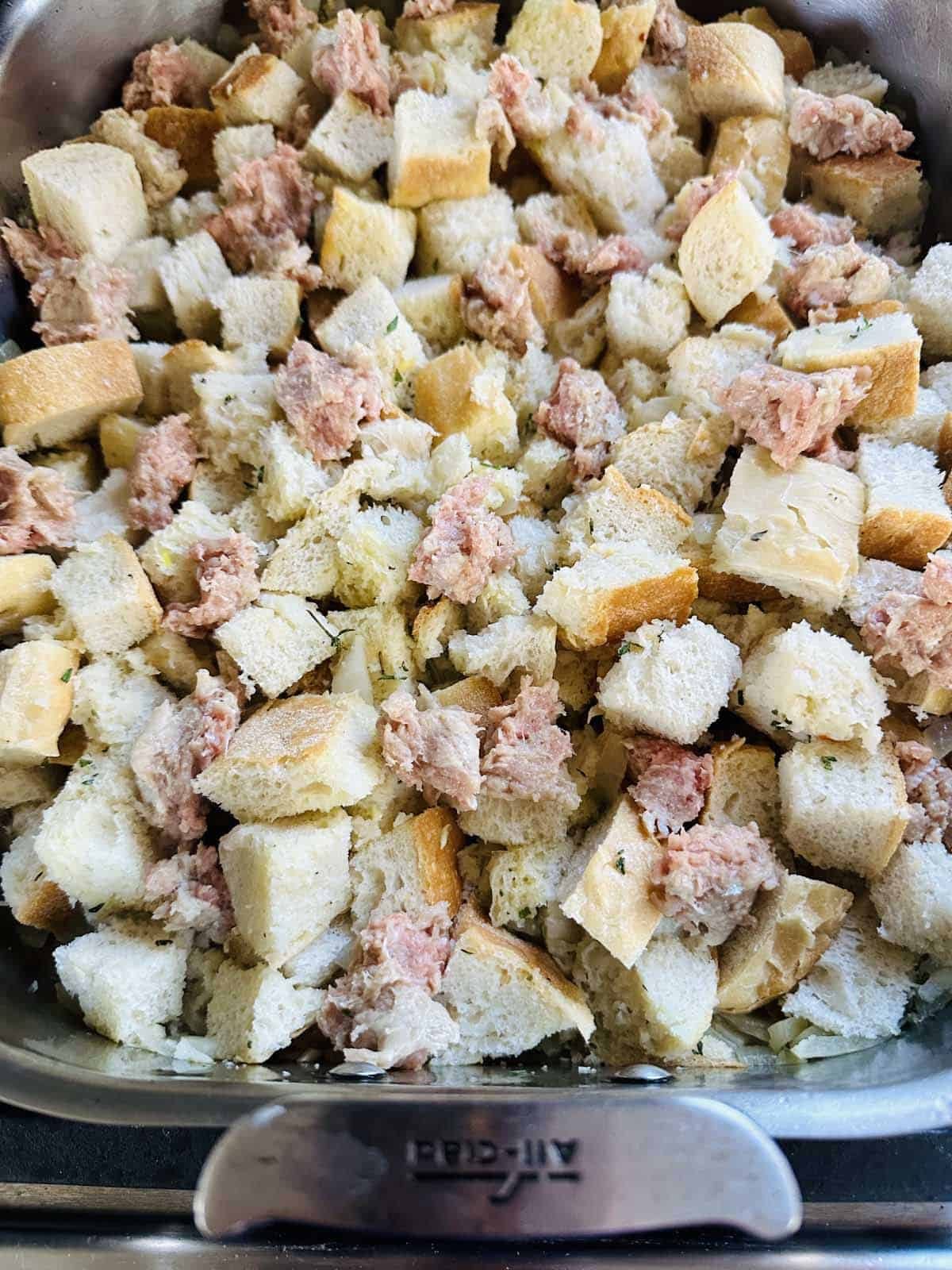 A metal baking dish filled with cubed bread and small portions of raw sausage meat, ready to be cooked or baked.