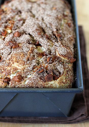 Close-up of a loaf of cinnamon bread topped with cinnamon sugar and nuts, freshly baked in a metal loaf pan.