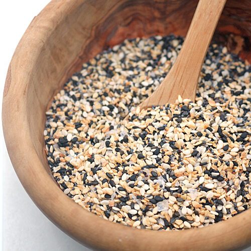 A wooden bowl filled with a mixture of black and white sesame seeds and a wooden spoon resting inside.