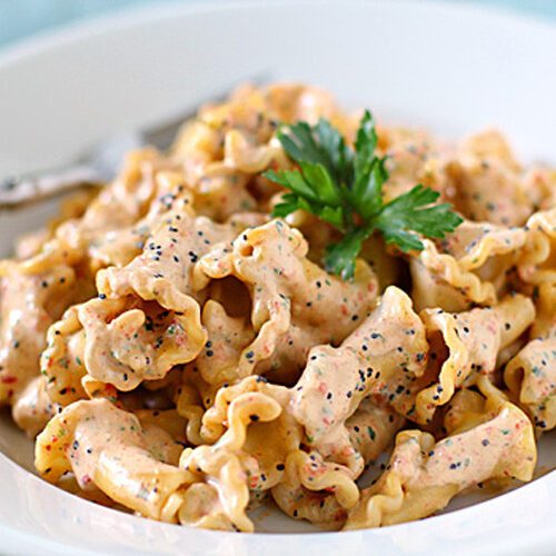 A plate of mafaldine pasta coated in a creamy sauce, garnished with fresh parsley and sprinkled with black pepper, with a fork resting on the side.