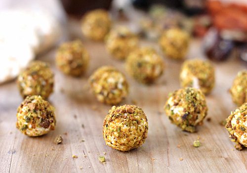 Several small, round cheese balls coated in chopped nuts are scattered on a wooden surface. The background is slightly blurred, highlighting the texture and detail of the cheese balls in the foreground.