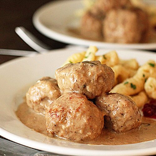 A plate of Swedish meatballs in creamy brown gravy, served with a side of spaetzle pasta and a dollop of lingonberry sauce.