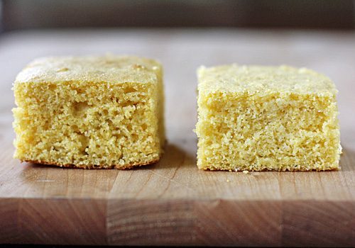 Two pieces of cornbread sit side by side on a wooden surface, each showing a slightly different texture and height. The cornbread on the left is thicker and more crumbly, while the one on the right is denser and shorter.