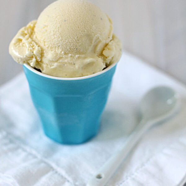 A scoop of vanilla ice cream in a blue cup sits on a folded white cloth napkin, with a white spoon placed beside it.