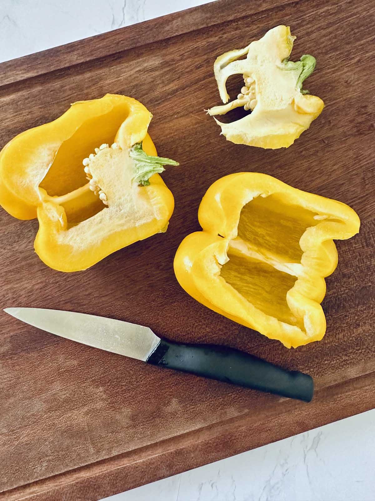 A yellow bell pepper cut into halves and quarters sits on a wooden cutting board next to a black-handled knife.